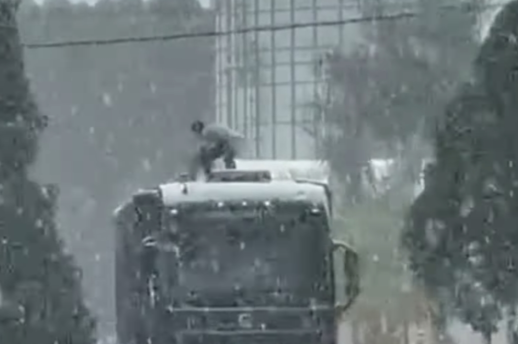 Caminhoneiro cobre carga embaixo de chuva enquanto colegas filmam sem ajudar
